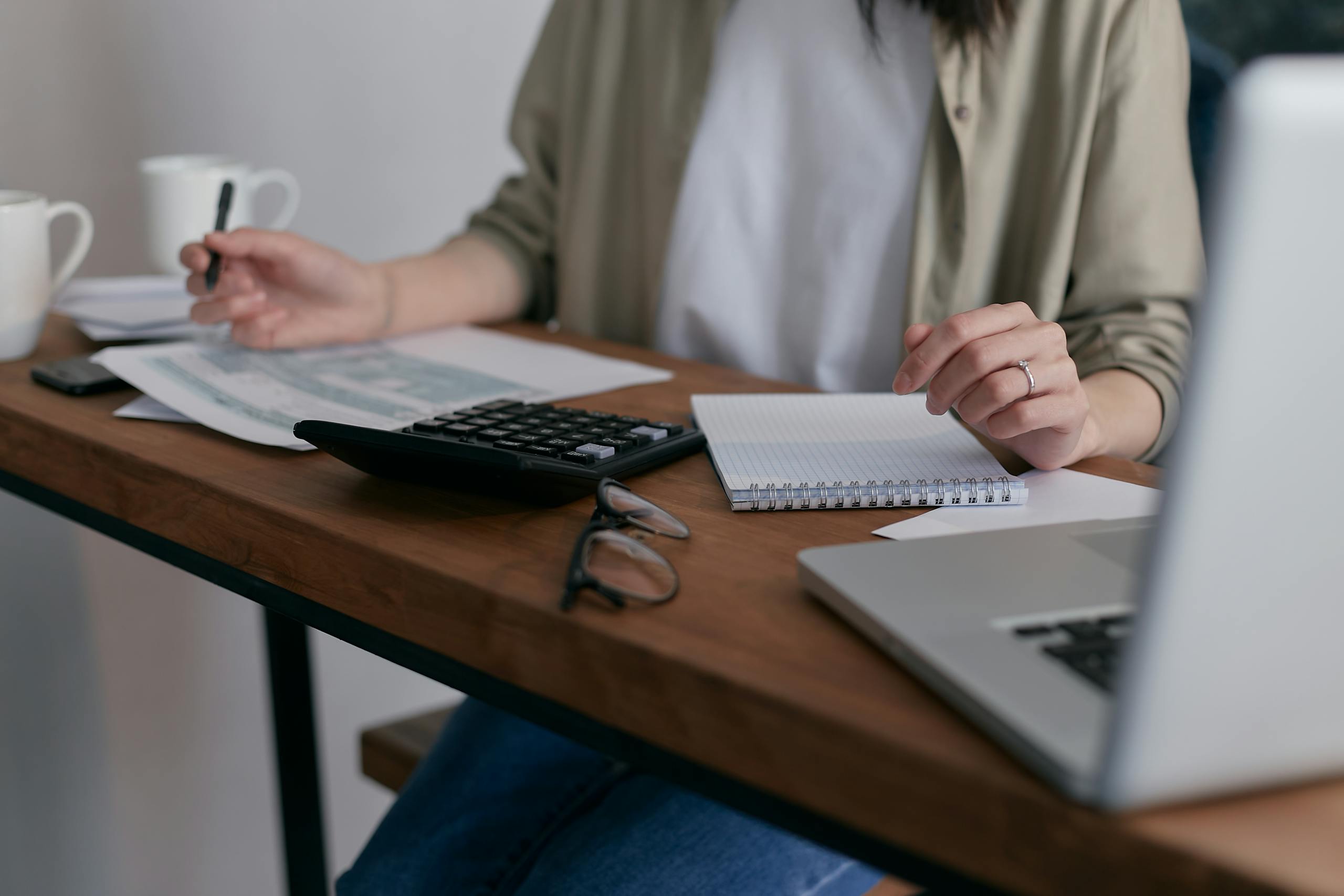 Woman managing finances at home using laptop and calculator on wooden desk.