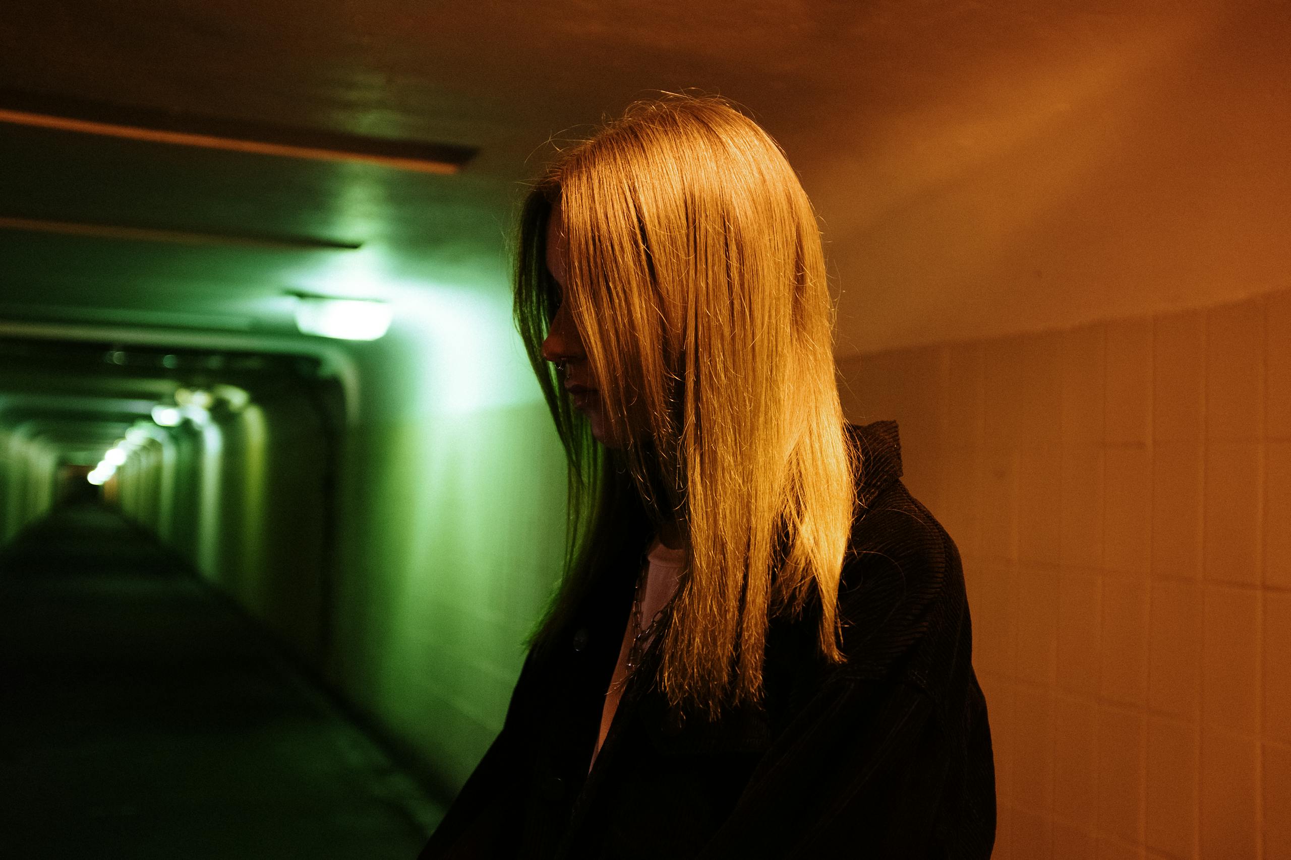 Woman stands in dimly lit urban underpass with contrasting neon lights casting dramatic shadows