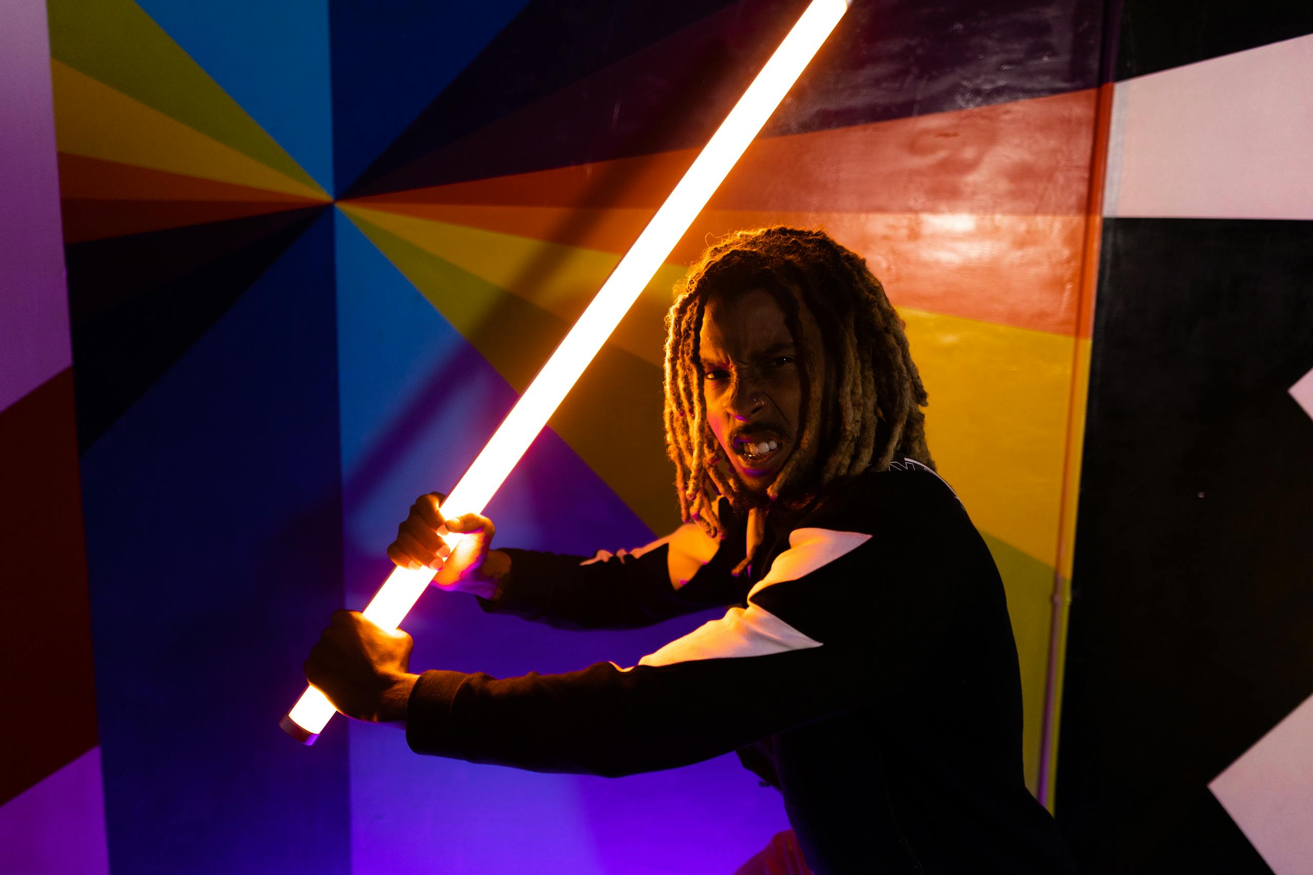 Young adult posing energetically with glowing neon sword against colorful geometric backdrop.