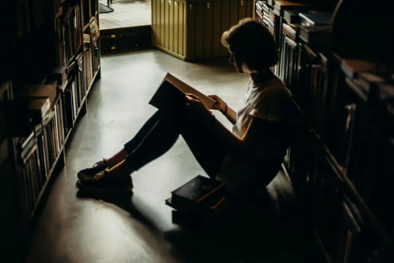 Young woman engrossed in book sitting on floor of quiet library creating cozy reading atmosphere