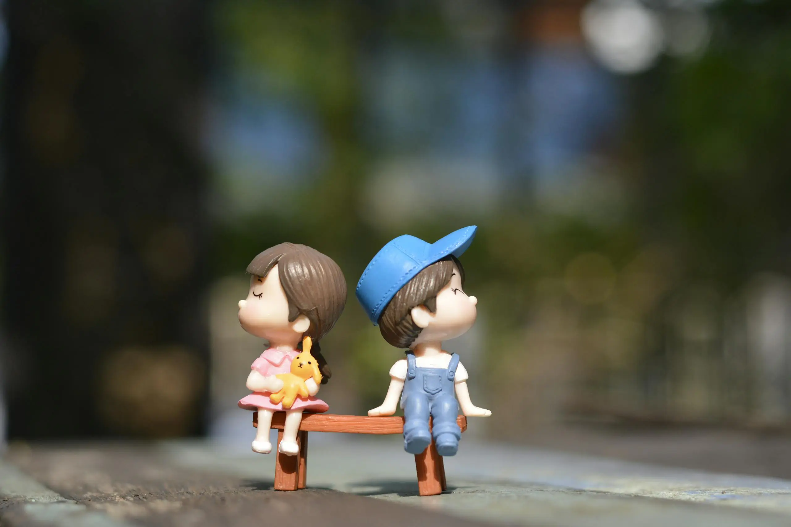 Decorative figurines of boy and girl sitting together on sunny bench.