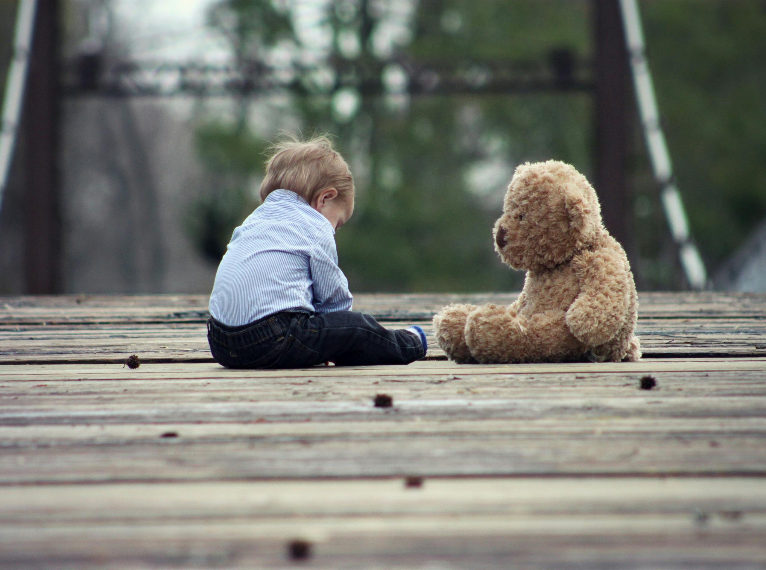 Adorable toddler sitting with teddy bear on wooden bridge enjoying peaceful moment outdoors