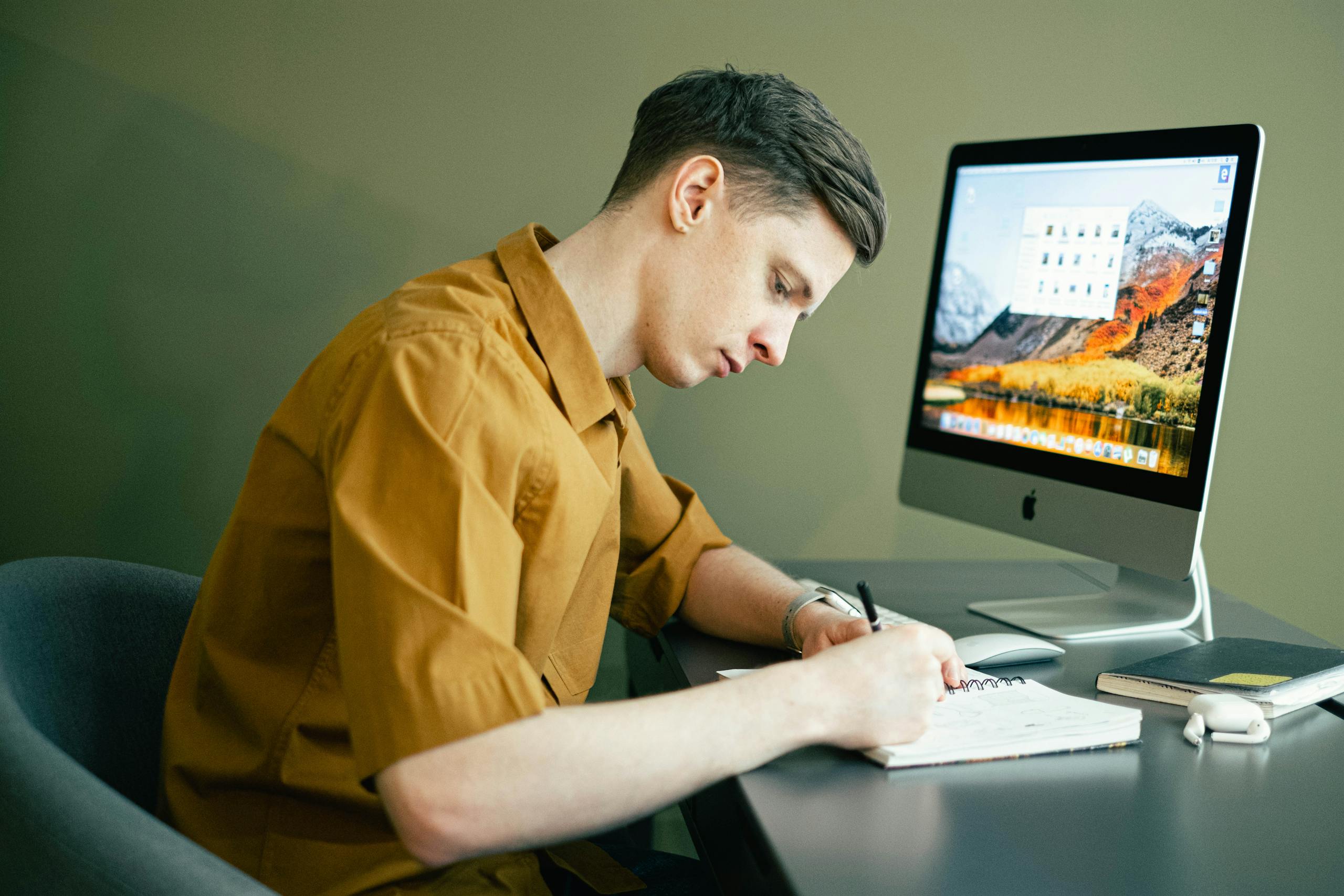 Adult male concentrating on notes with desktop computer in home office setting