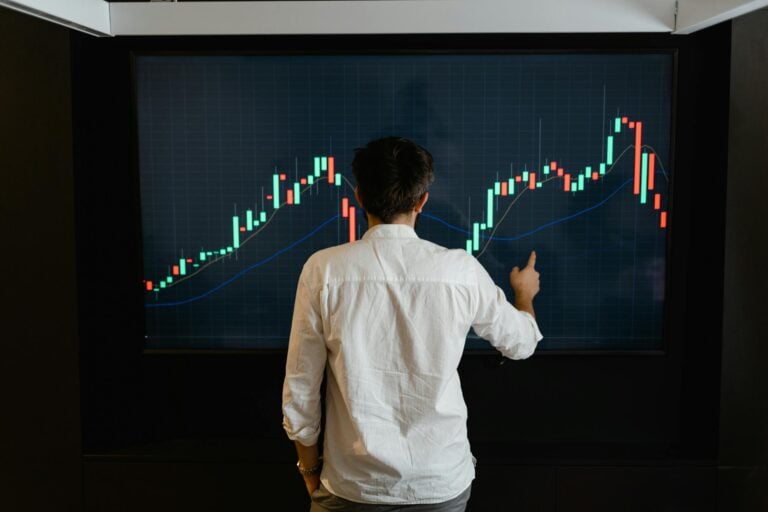 Adult male reviewing stock market data on large display screen indoors.