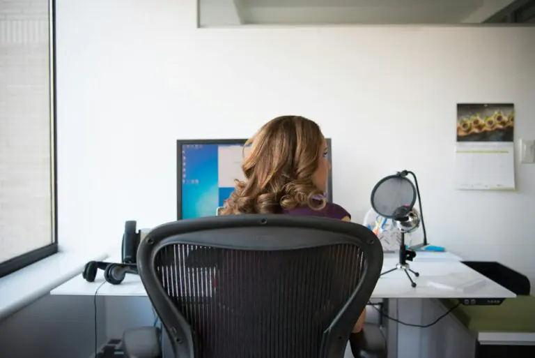 Adult woman in office with computer and microphone focused on work.