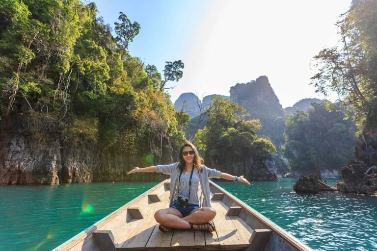 Asian woman enjoying serene boat journey through lush karst landscape of Thailand.
