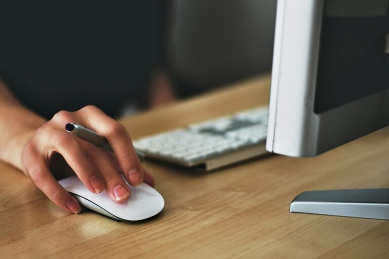 Person's hand using white computer mouse at wooden desk workspace