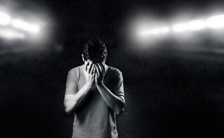 Black and white photo of man covering face expressing emotion and solitude