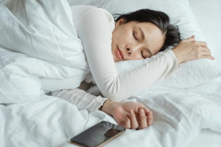 Calm Asian woman in white pajamas sleeping peacefully in comfortable bed.