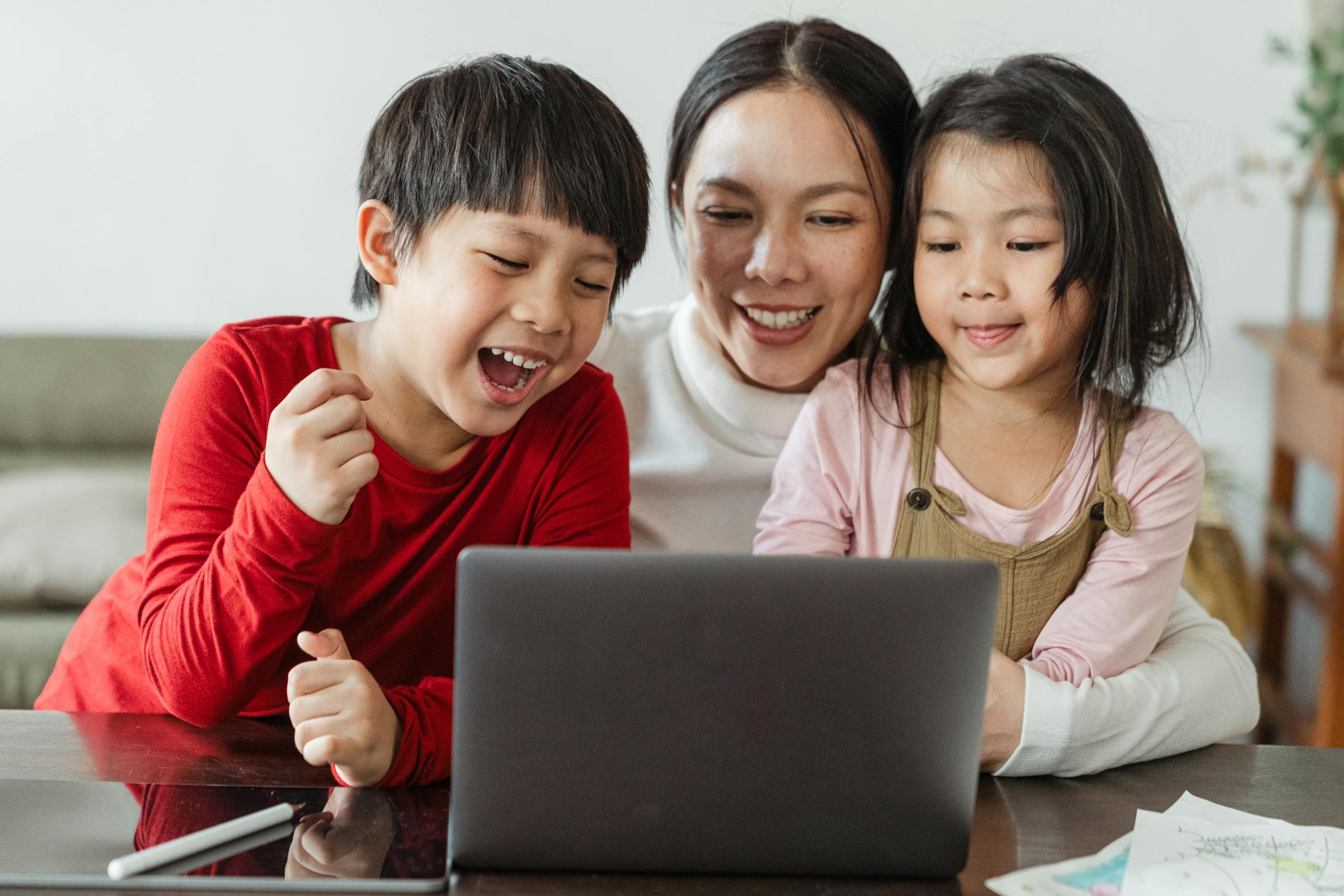Happy Asian family laughing together watching video on laptop during weekend