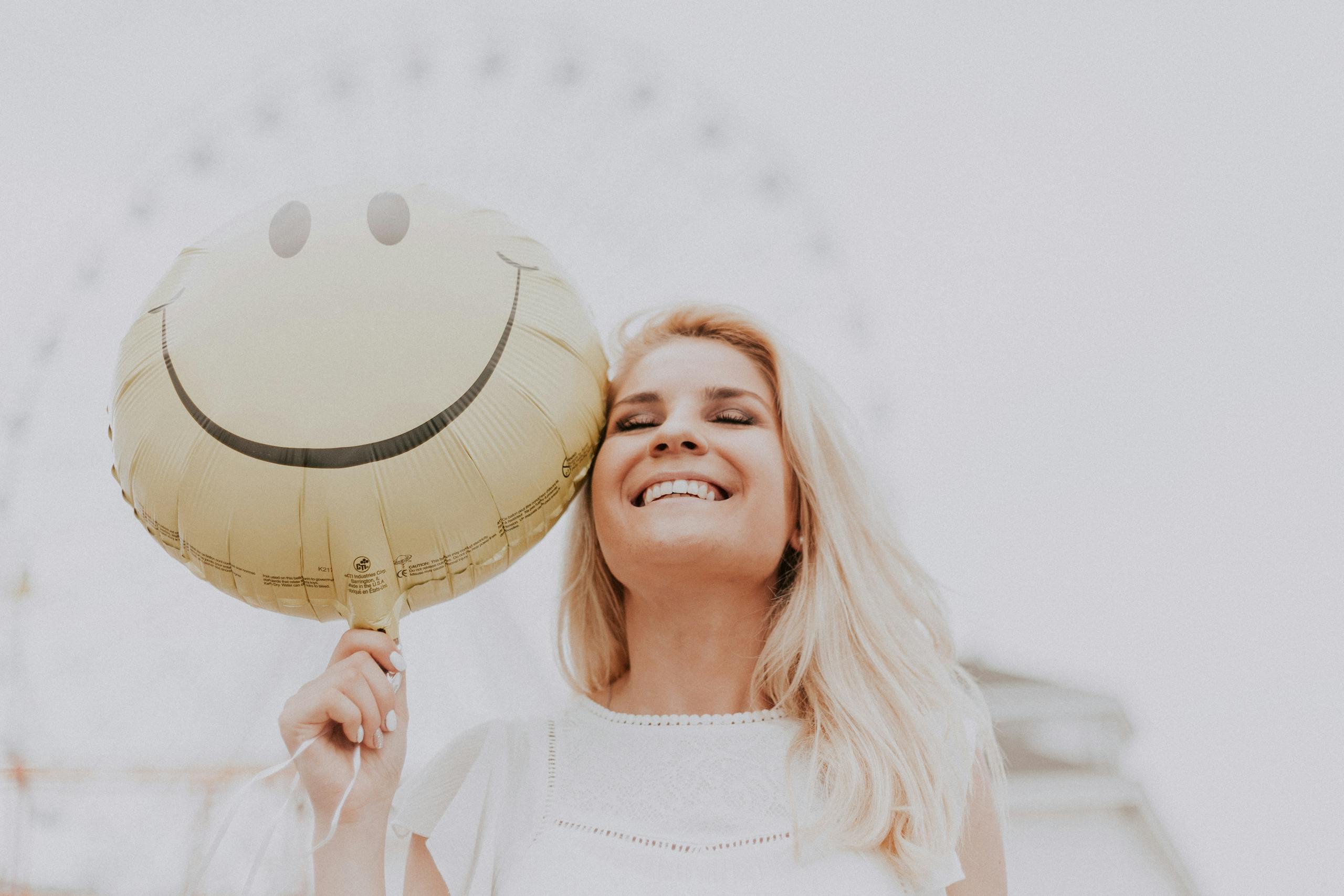 Cheerful woman holding smiley balloon outdoors on sunny day exuding happiness