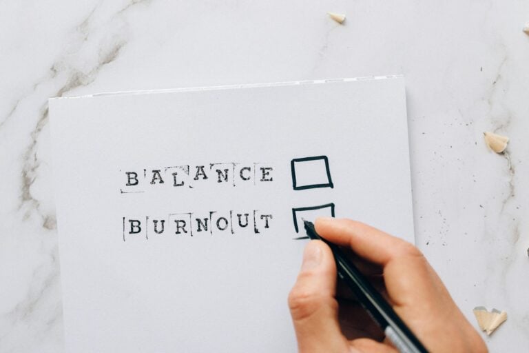 Hand hovering over checklist with balance or burnout options symbolizing stress and choice