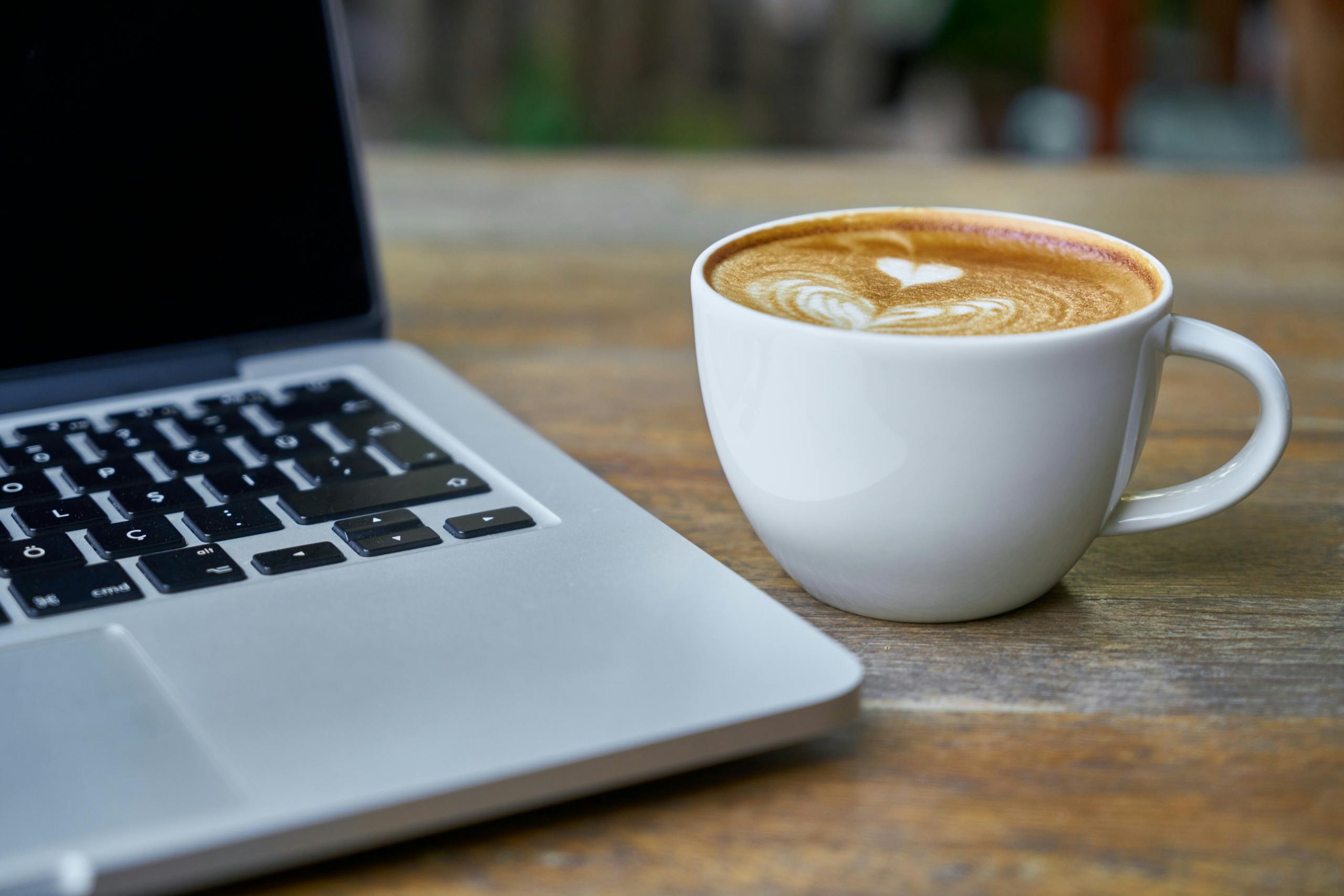 Latte with latte art beside laptop on rustic wooden table at home