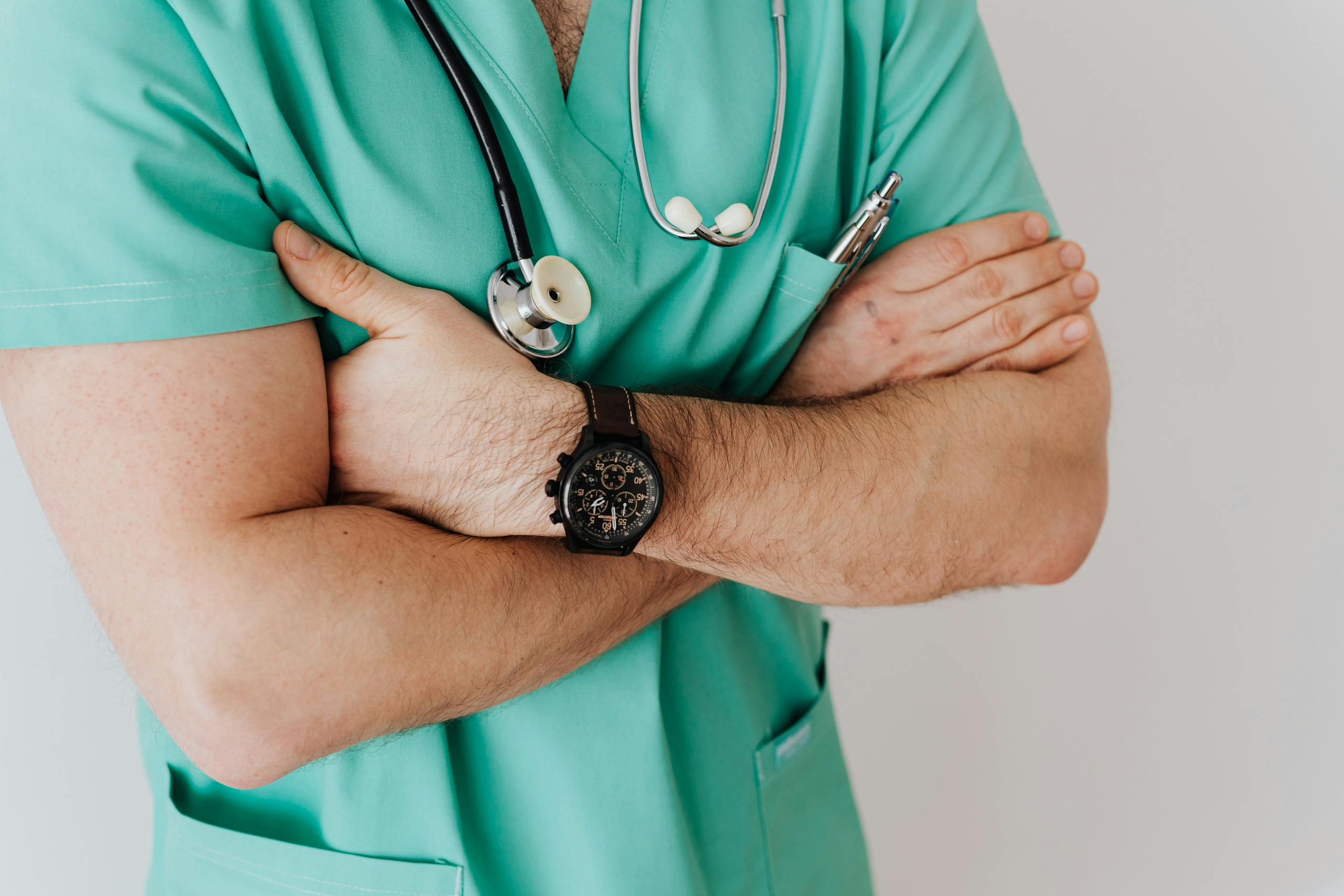 Male doctor in scrubs with stethoscope arms crossed confidently