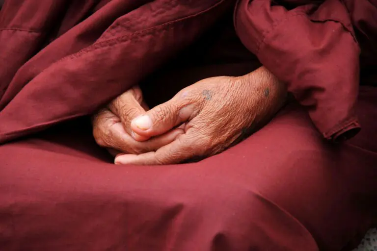 Close-up of monk's hands in prayer wrapped in maroon robe symbolizing spirituality