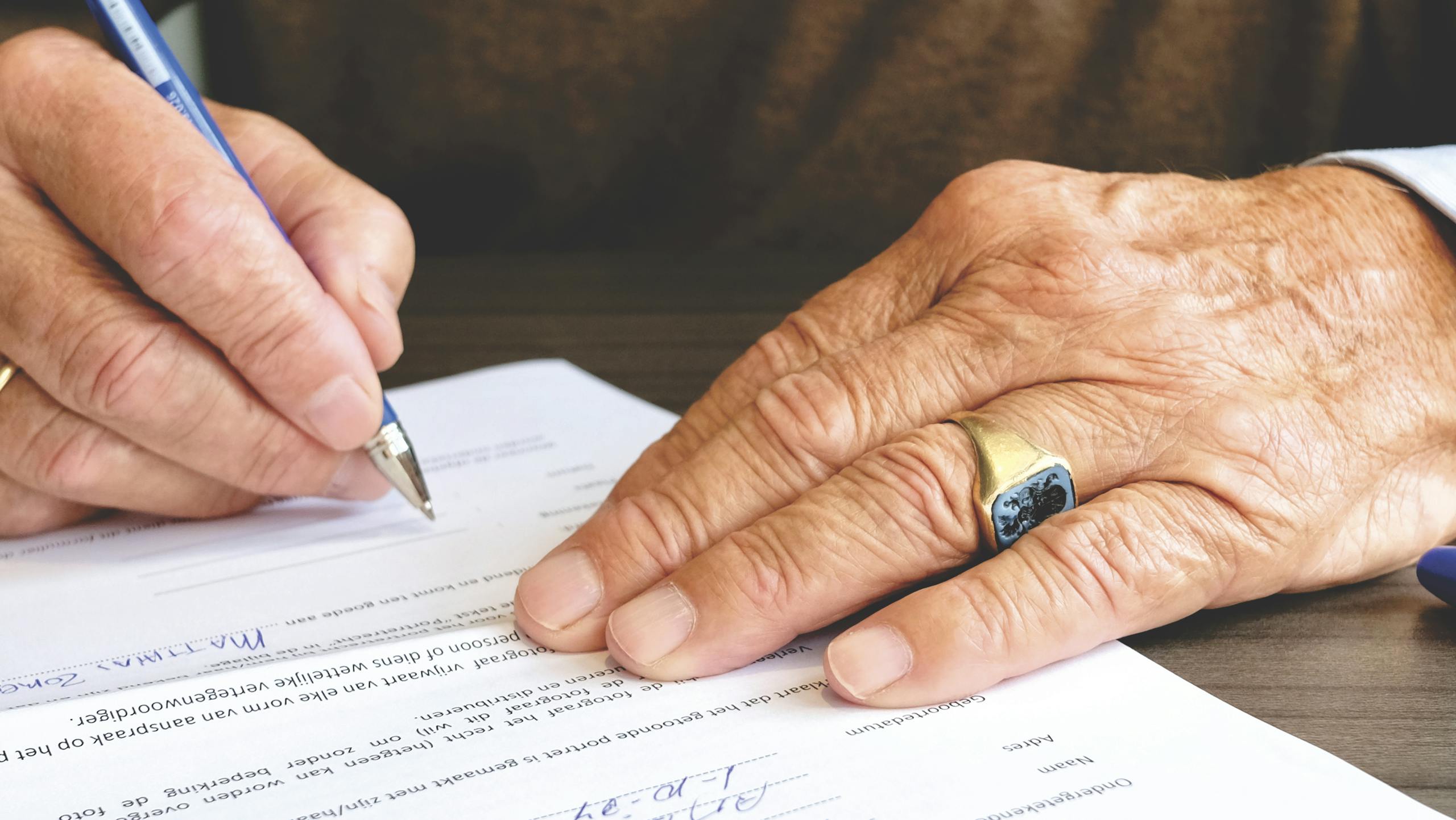 Senior adult signing legal document close-up with hand and gold ring.