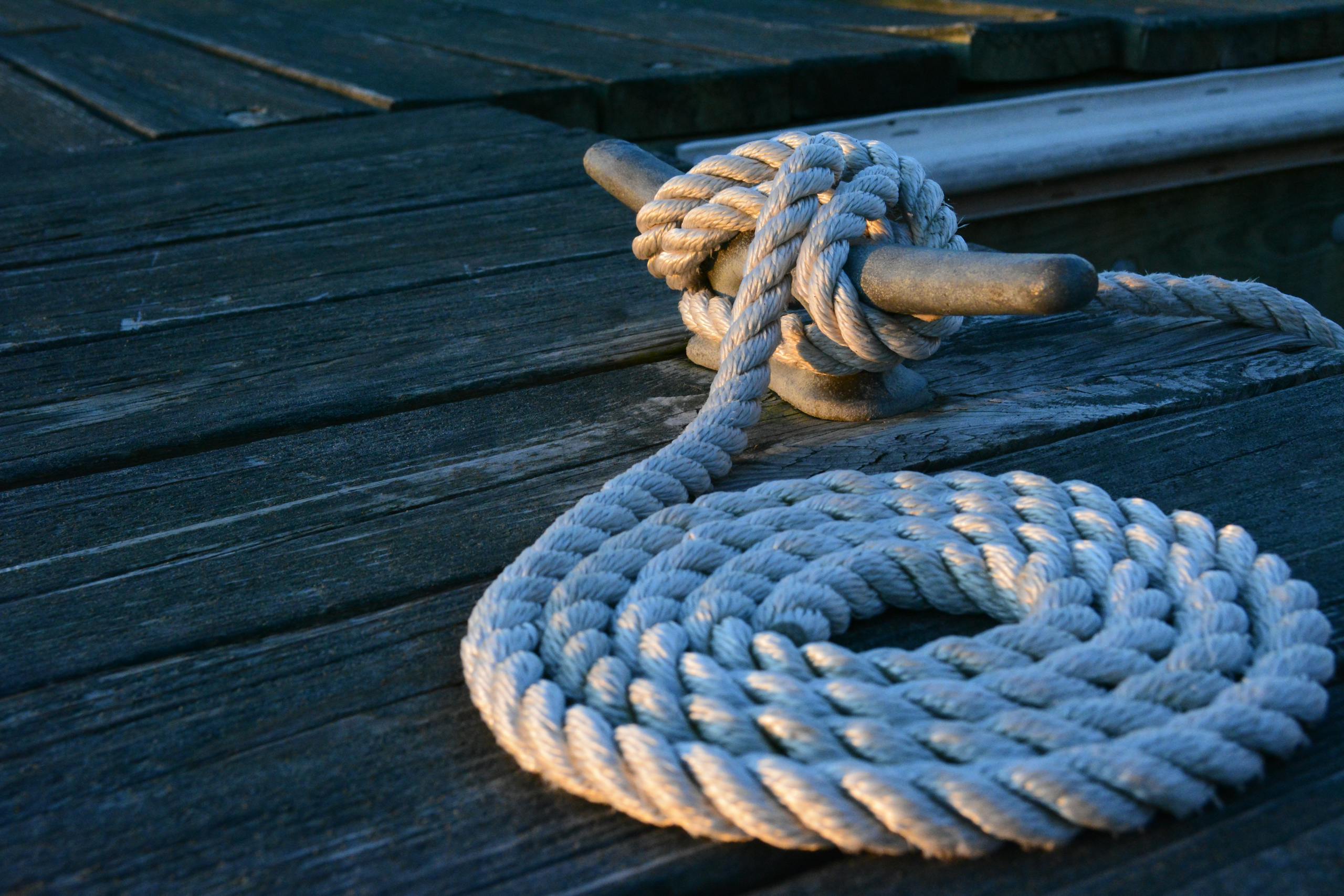 Sturdy nautical knot on weathered wooden dock at sunset close up