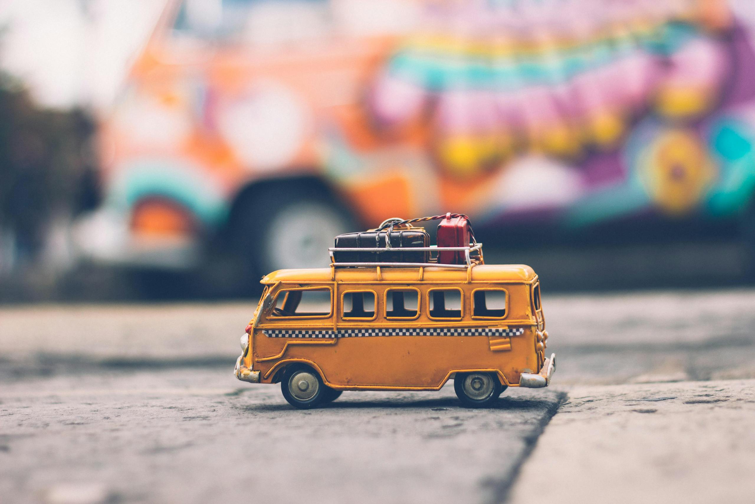 Toy Volkswagen van with luggage against colorful street backdrop.