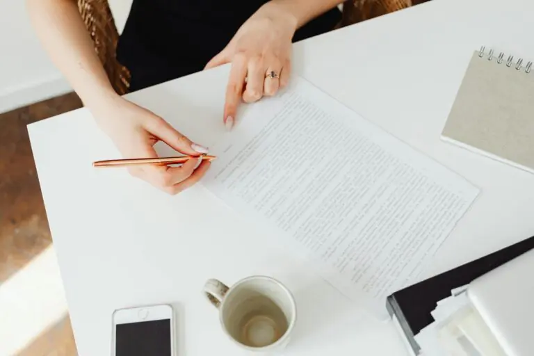 Close-up of woman reviewing document at white desk with pen