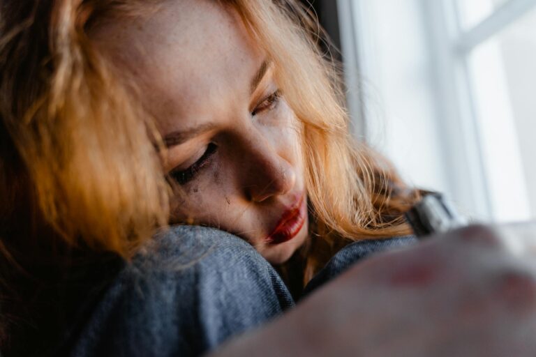 Close-up of woman with red hair in thoughtful, emotional moment indoors.