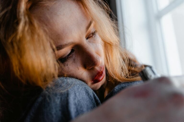 Close-up of woman with red hair in thoughtful, emotional moment indoors.
