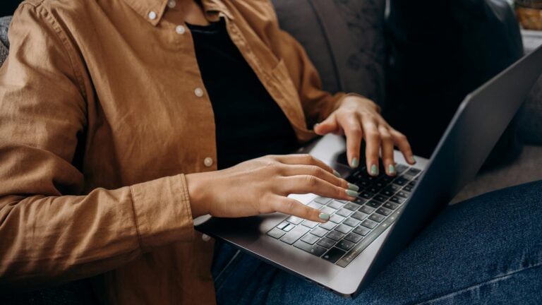 Close-up of hands typing on laptop keyboard while wearing brown casual shirt