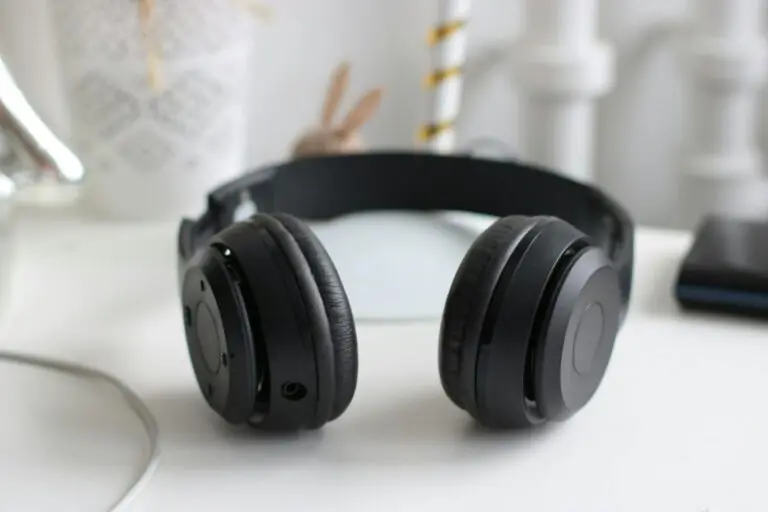 Black wireless headphones on white desk in modern minimalist setting.