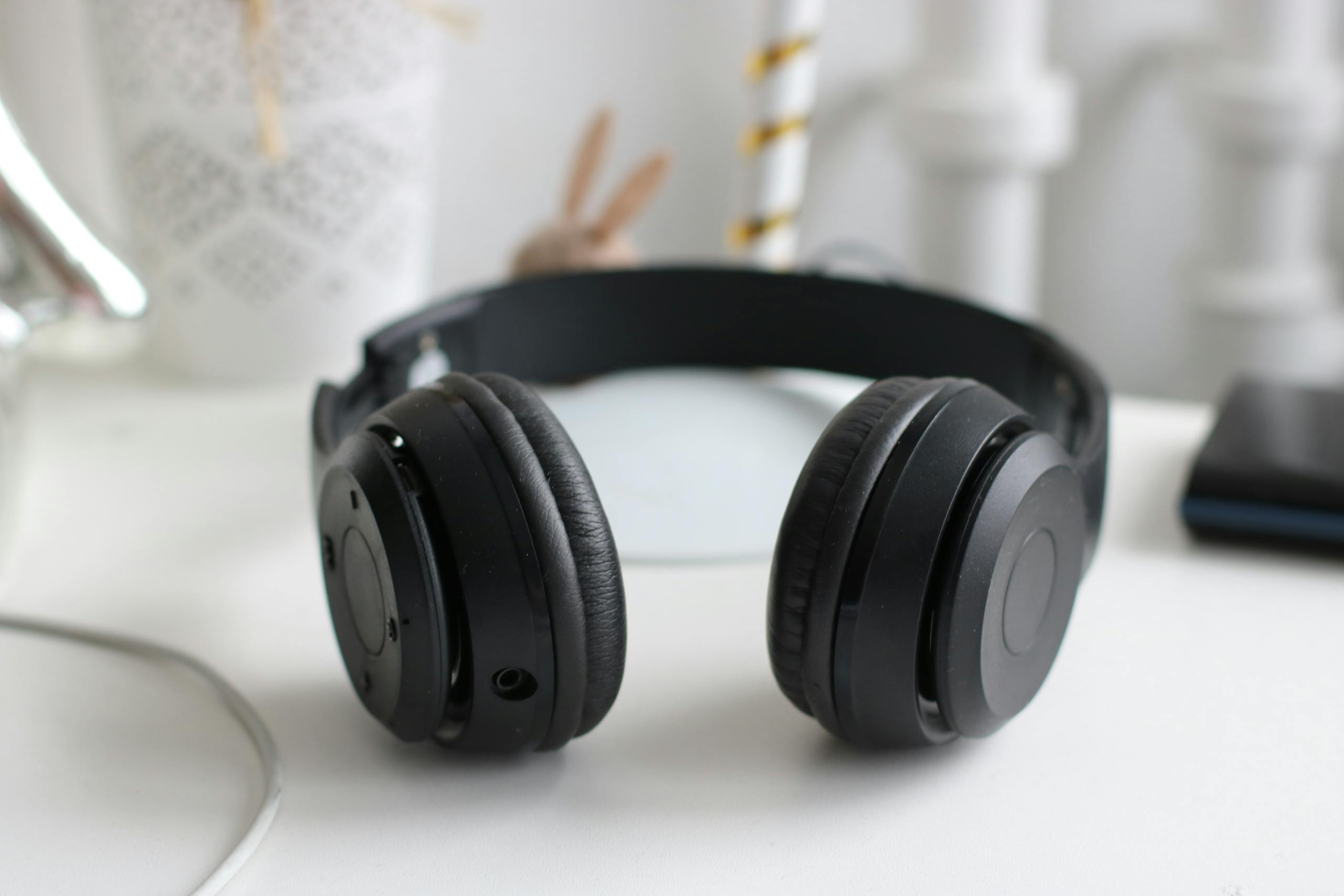 Black wireless headphones on white desk in modern minimalist setting.