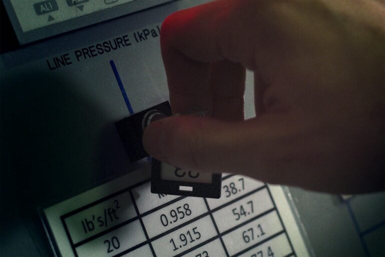 Close-up of hand adjusting pressure gauge dial in industrial setting.