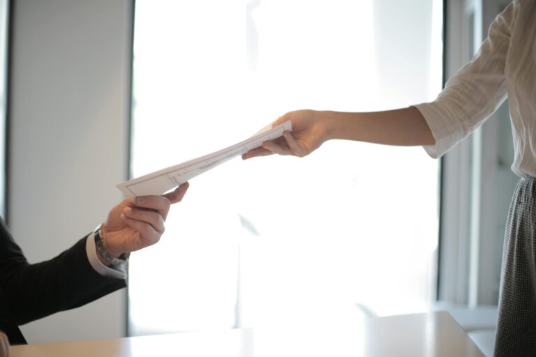 Close-up of hands exchanging business documents in professional office setting.