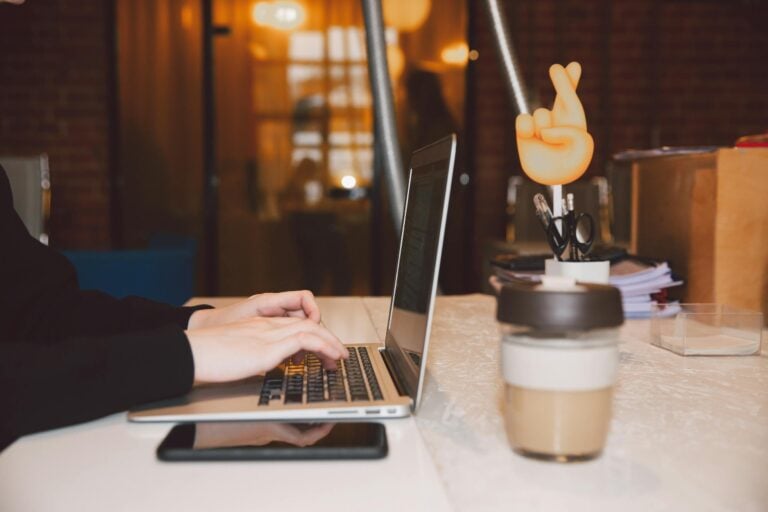 Close up of hands typing on laptop in modern office with coffee and creative decor.