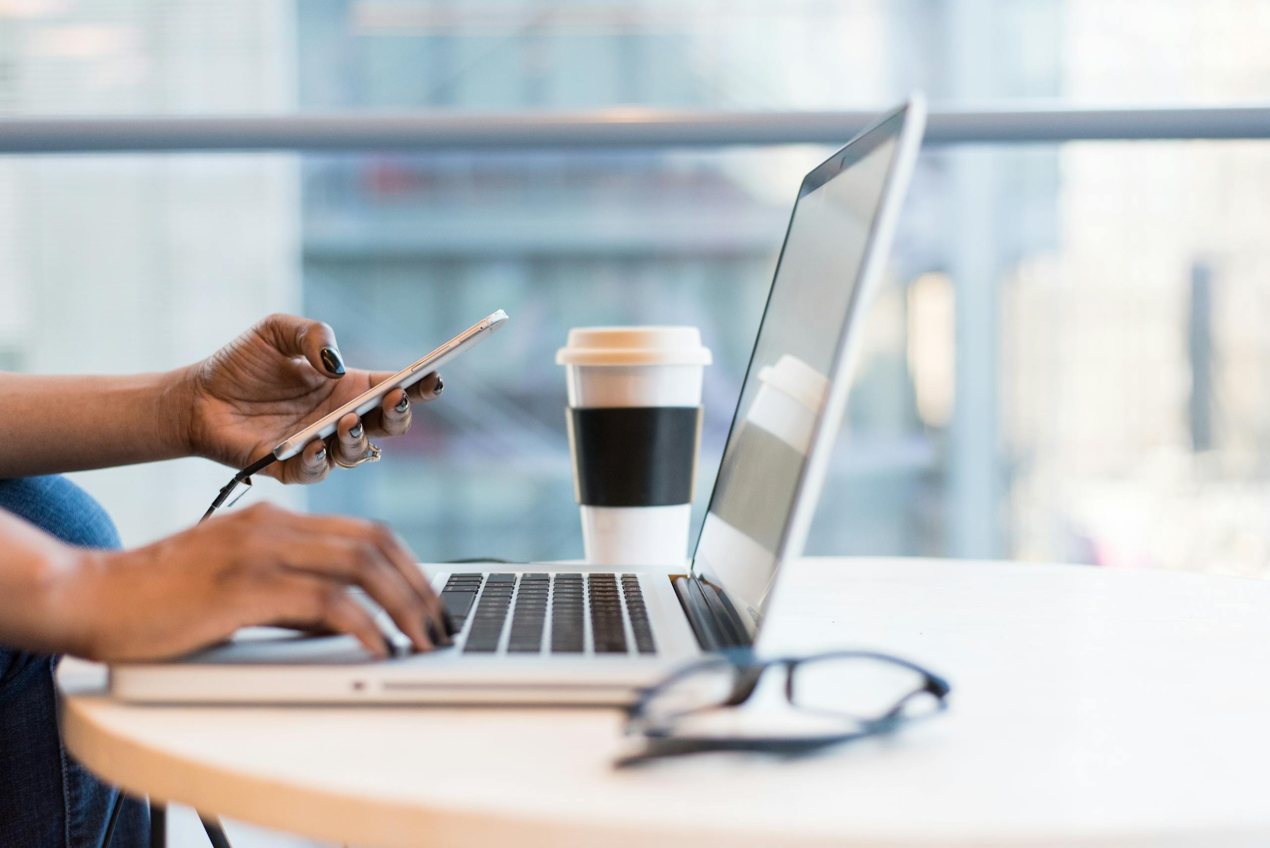 Close up of hands using laptop and phone with coffee on desk