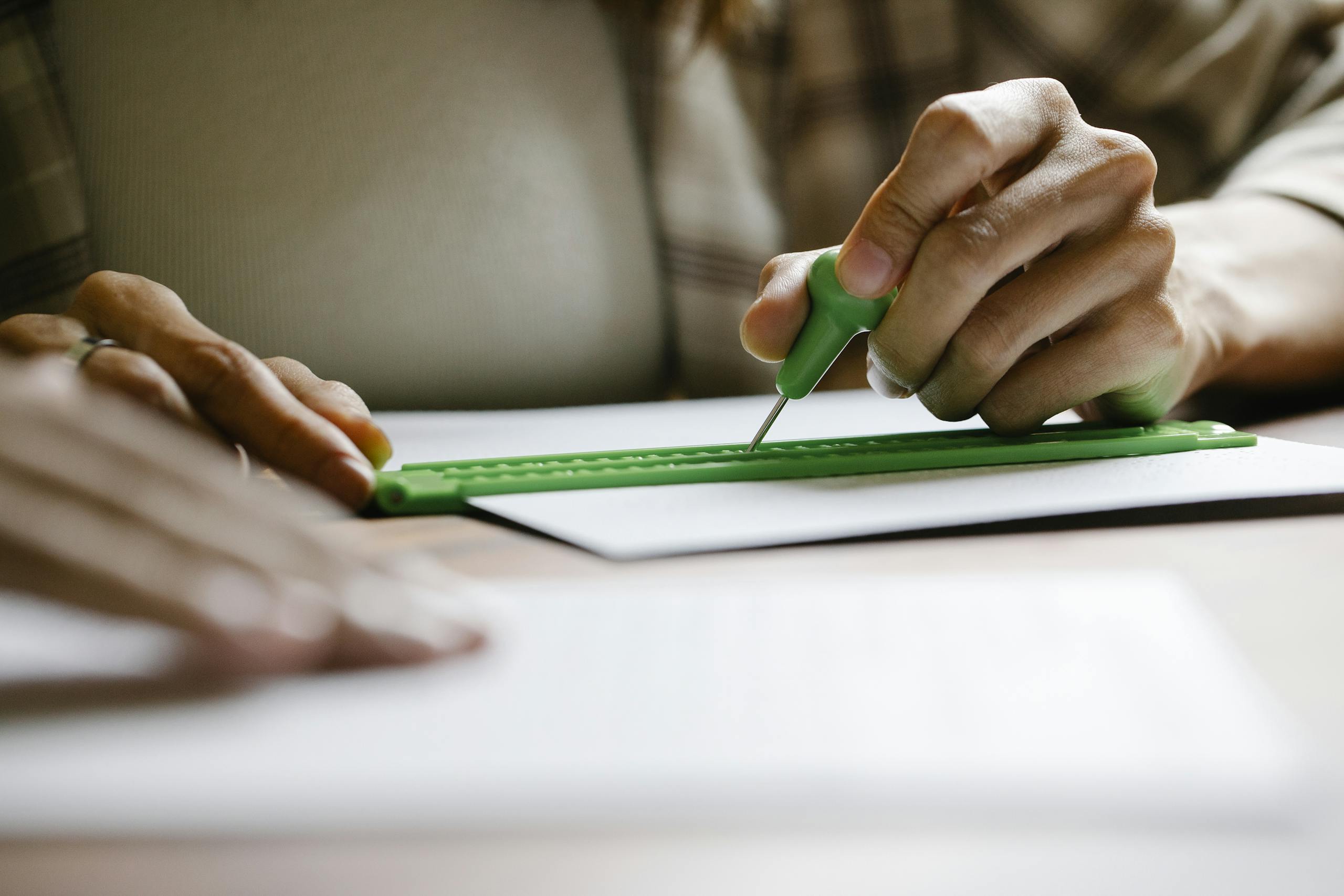 Close up of hands using stylus and ruler to write braille on paper, inclusive education.