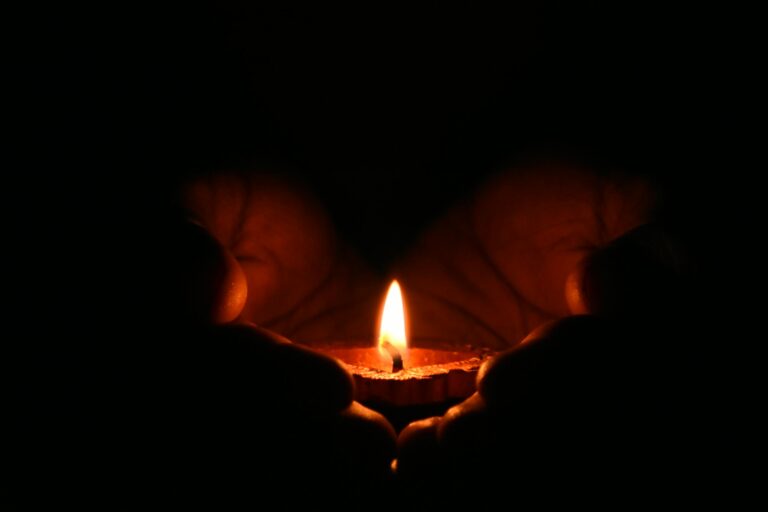 Close-up of hands warmly embracing lit candle in dark creating cozy atmosphere.