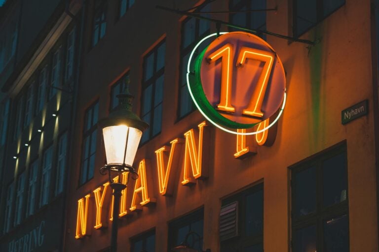 Colorful neon signs illuminate historic Nyhavn district in Copenhagen, Denmark.