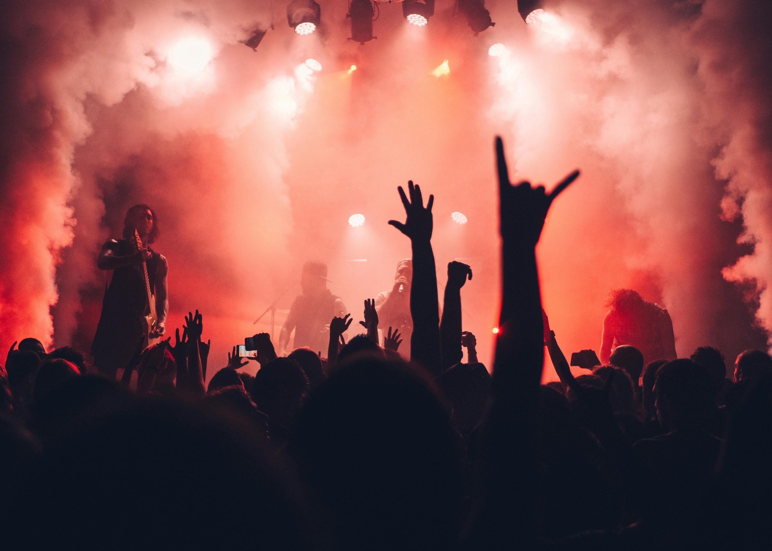 Silhouetted crowd with raised hands at energetic red-lit concert venue