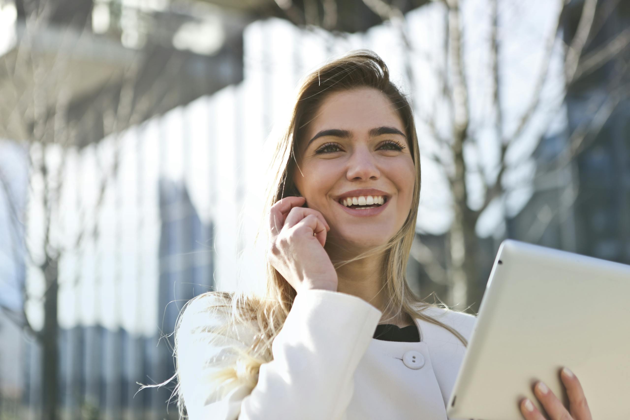 Confident businesswoman smiling while using tablet and phone outdoors in bright sunlight