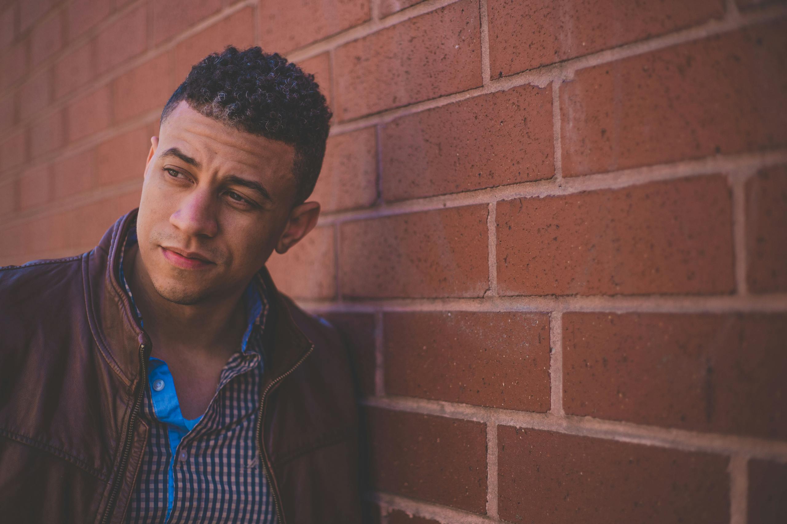 Confident male model in leather jacket against brick wall