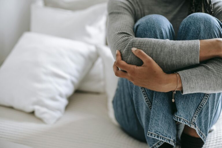 Faceless woman feeling helpless and frustrated with knees to chest on bed.