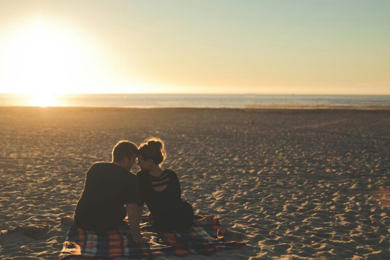 Two people sitting close together on beach at sunset, intimate moment
