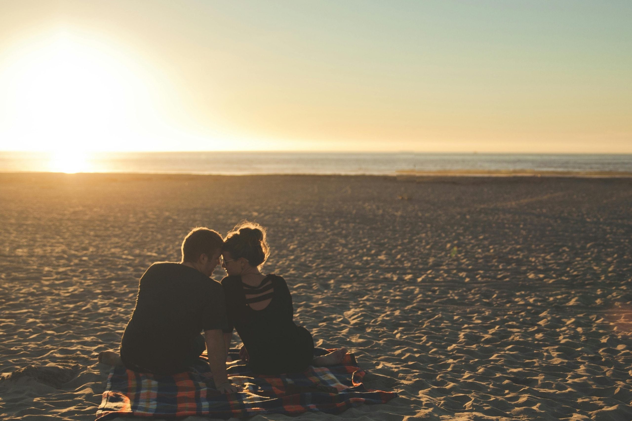 Two people sitting close together on beach at sunset, intimate moment