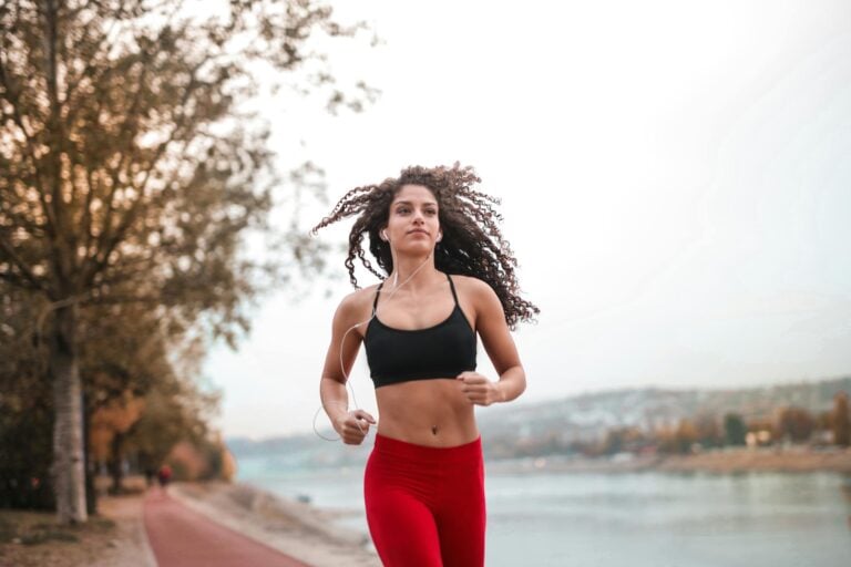 Determined woman in red leggings jogging along scenic riverside path embracing outdoor fitness.