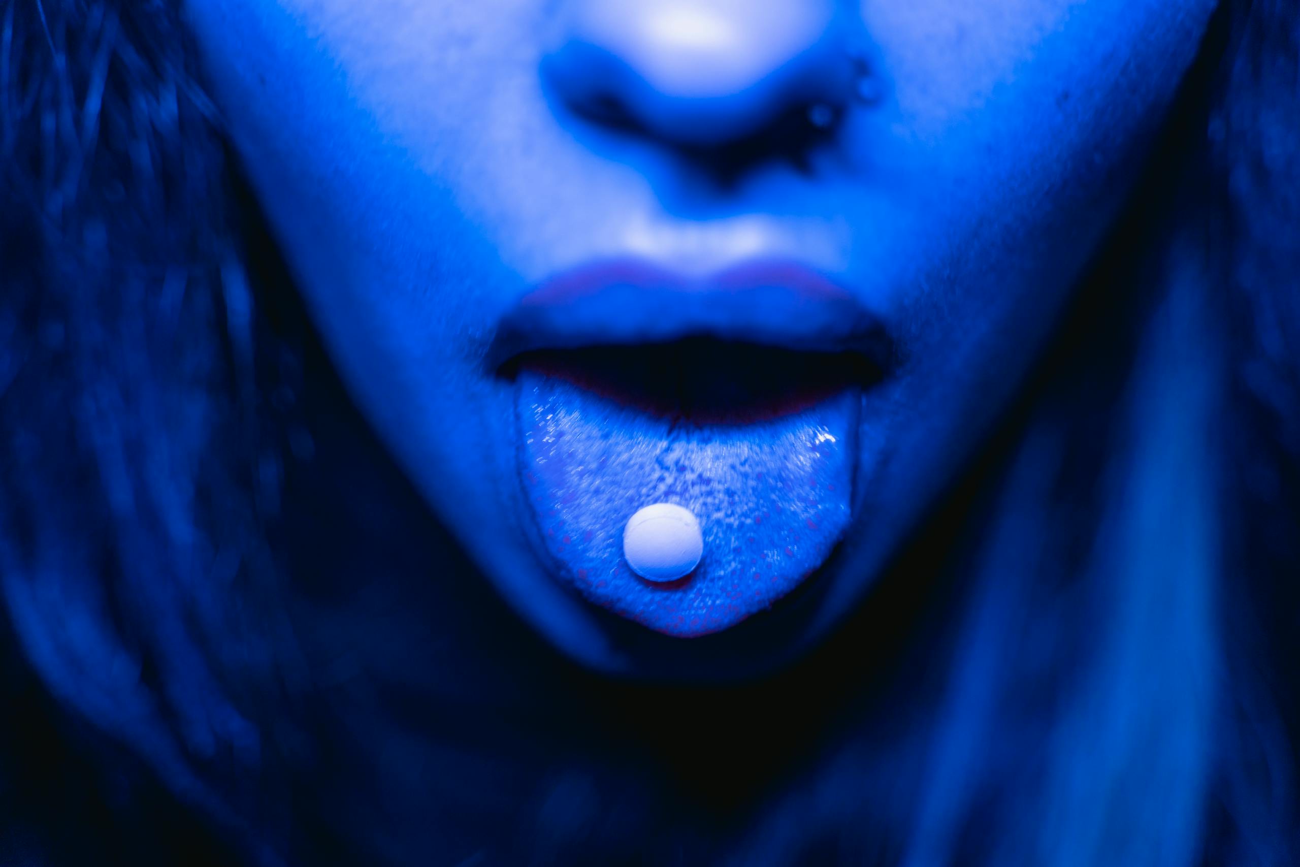 Dramatic close up of person with tablet on tongue in blue lighting