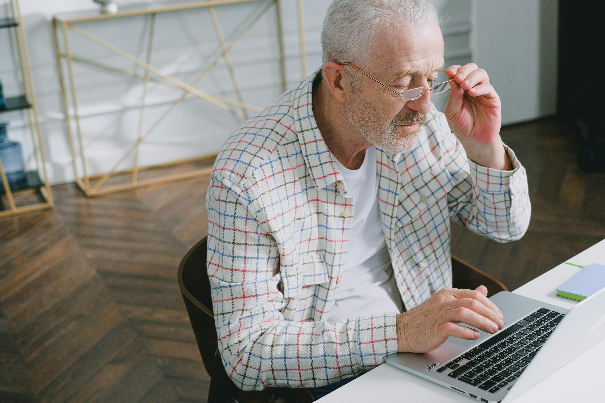 Elderly man wearing glasses focused on working at laptop indoors