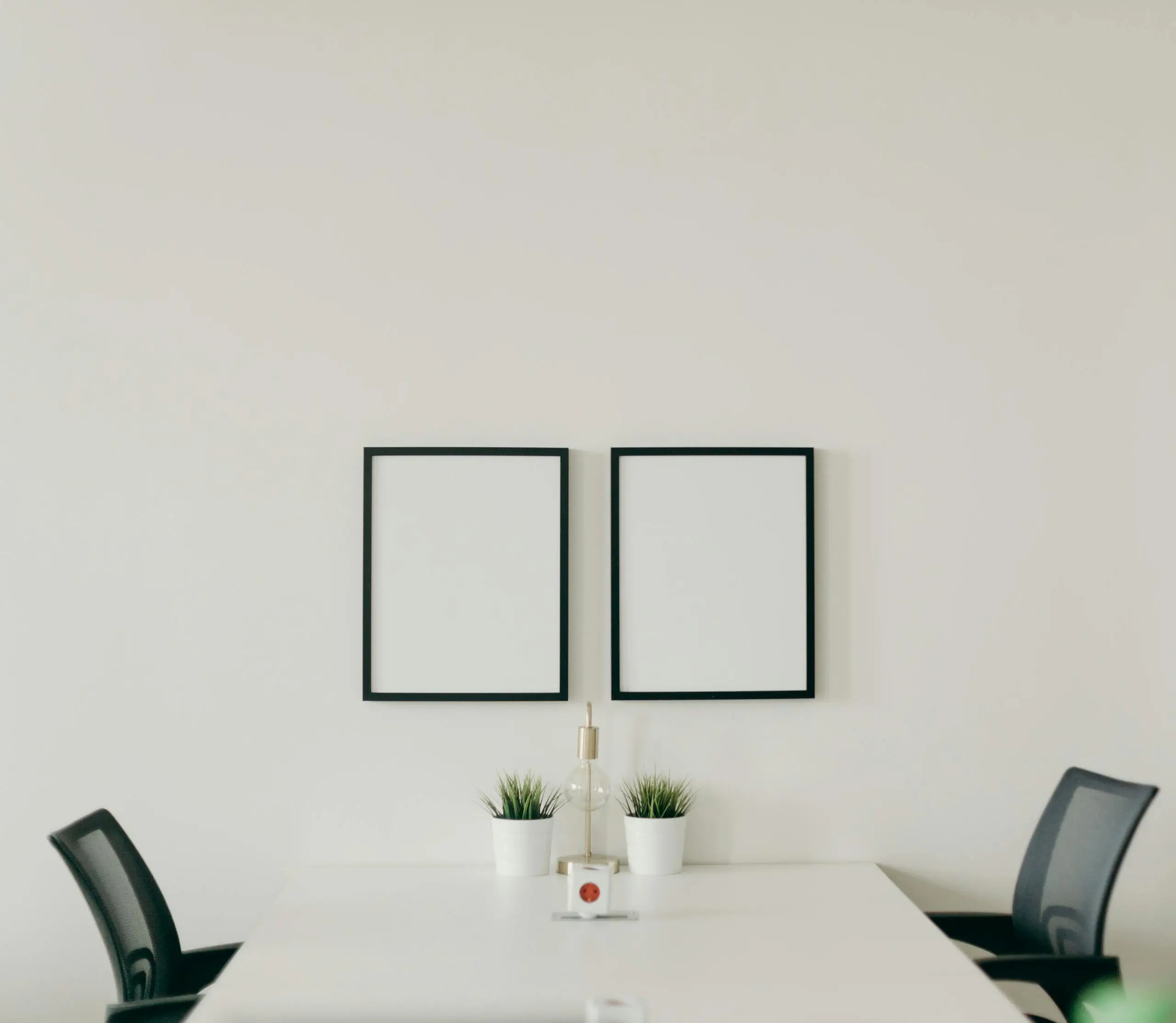 Minimalist home office with white desk, black chair, and decorative plants.