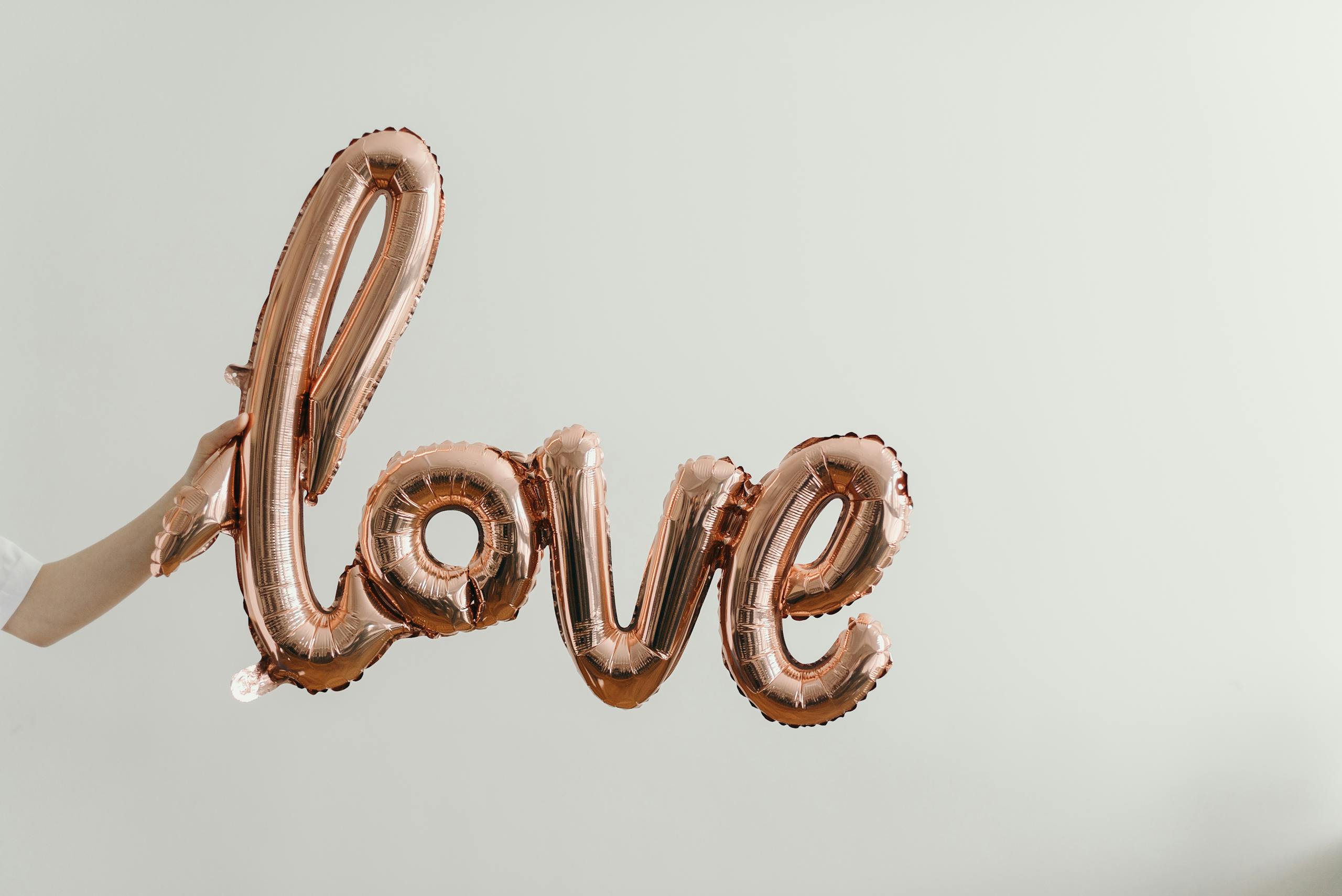 Elegant rose gold balloon spelling love on soft background.