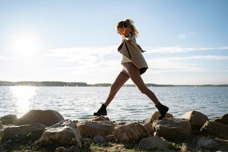 Woman jumping energetically across rocks by serene waterside during golden hour