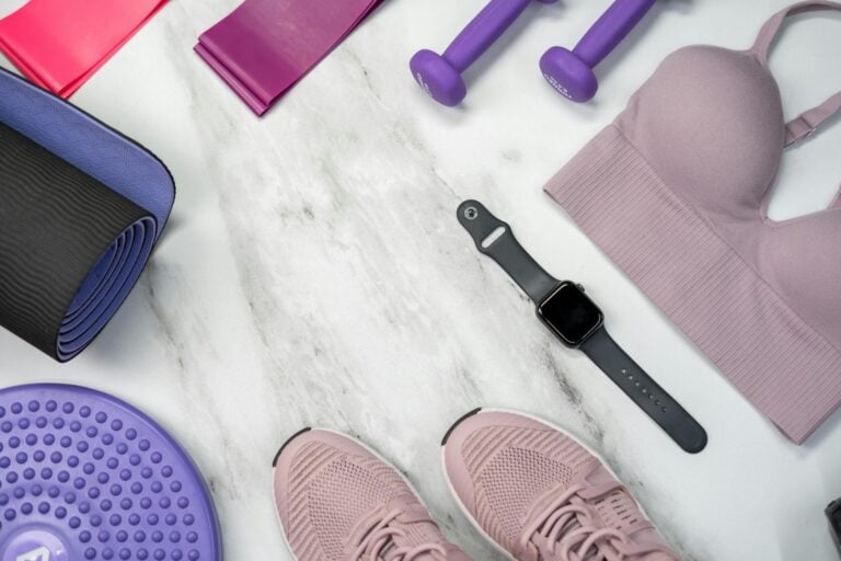 Flat lay of fitness equipment including yoga mat, dumbbells, and smartwatch on marble.