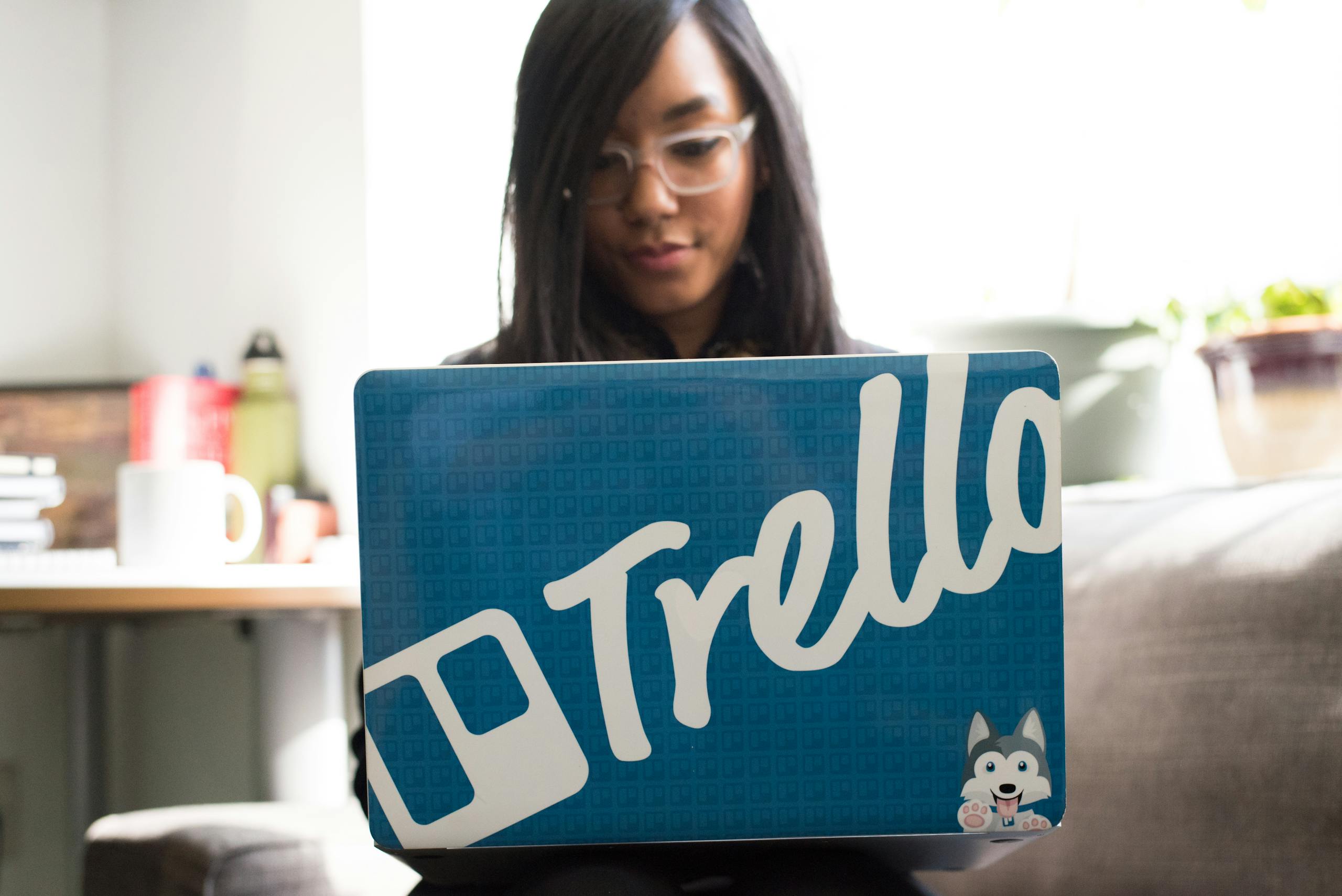 Focused woman engaged in remote work using trello branded laptop in cozy indoor setting.