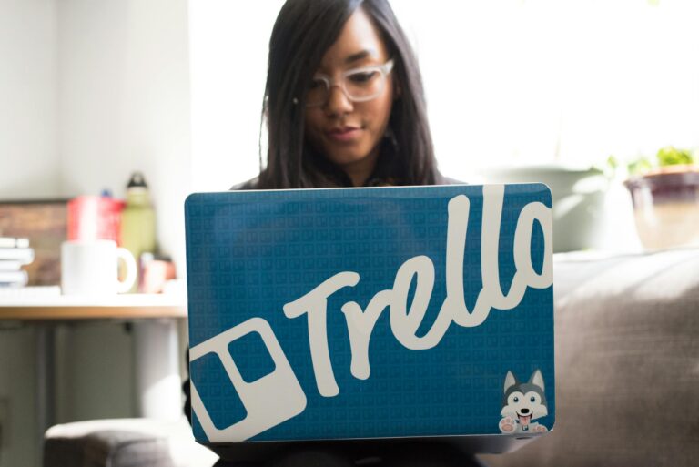 Focused woman engaged in remote work using trello branded laptop in cozy indoor setting.